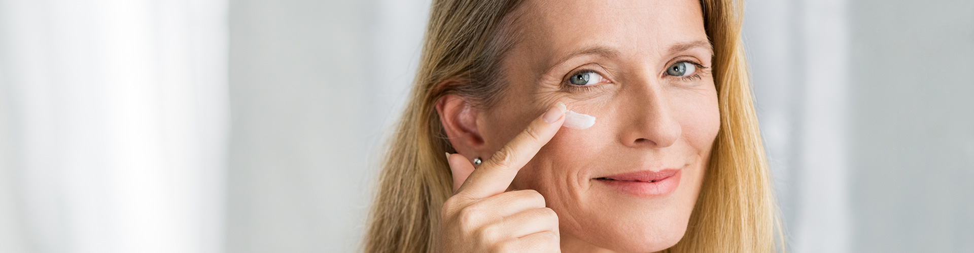 Hautberatung Frau vor dem Spiegel cremt sich Gesicht ein